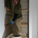 Dave working on interior construction of shipping container home, applying finish work to walls