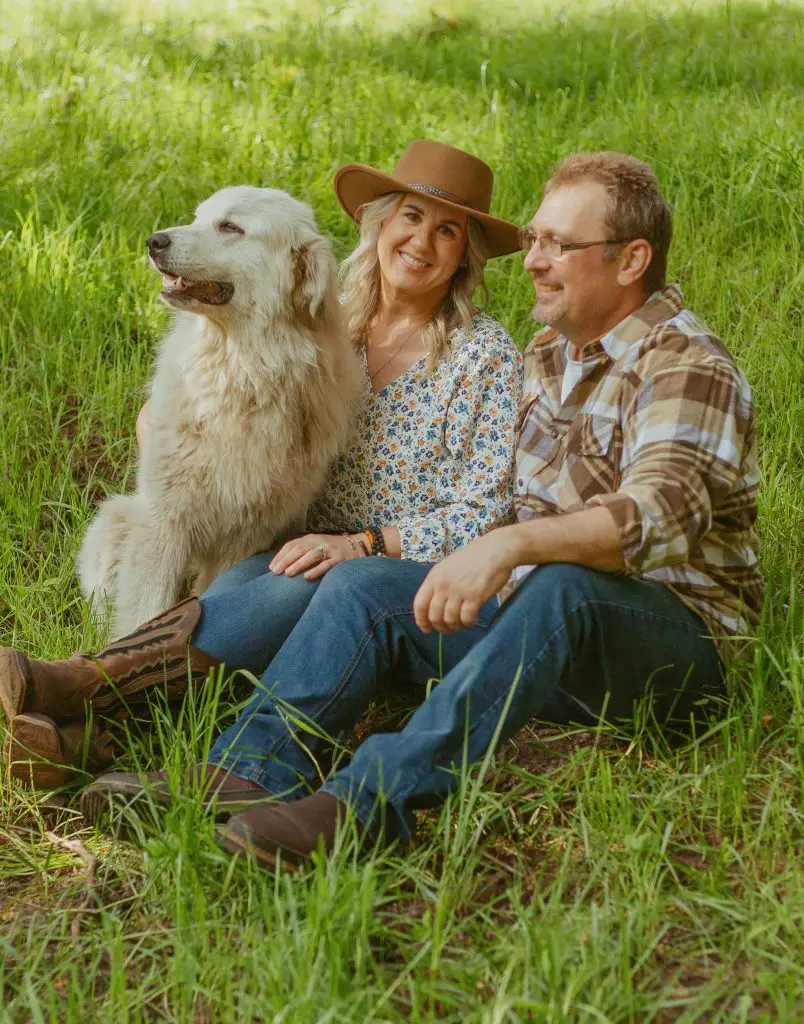 Jaimie and Dave Hinckle with their dog Chester sitting in green pasture at Highland & Co. Acres farm in Kalama, Washington