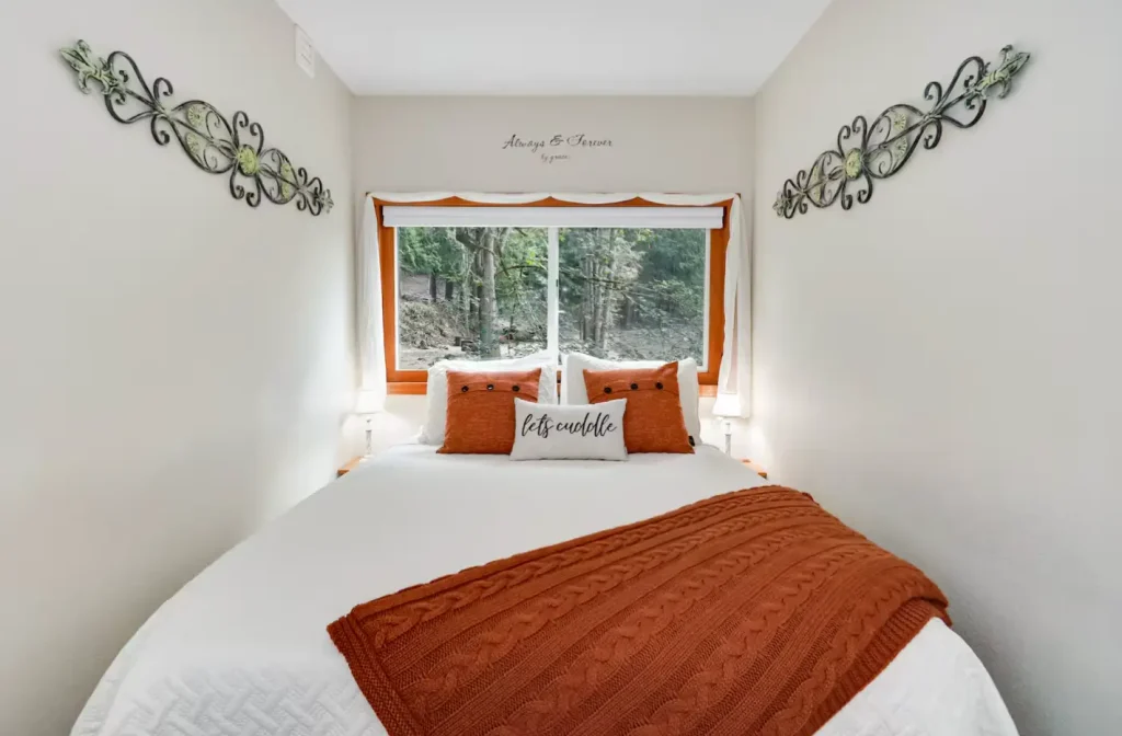 Cozy tiny home bedroom loft with queen bed, forest window views, and romantic 'let's cuddle' decor at Highland & Co. Acres