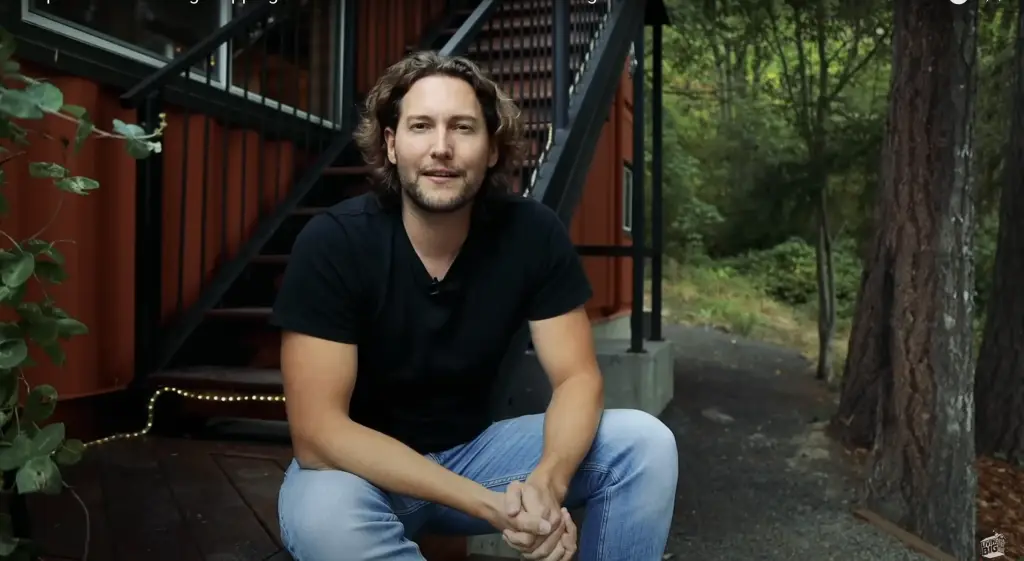 Dave from Highland & Co. Acres featured on Living Big in a Tiny House YouTube channel sitting outside shipping container home