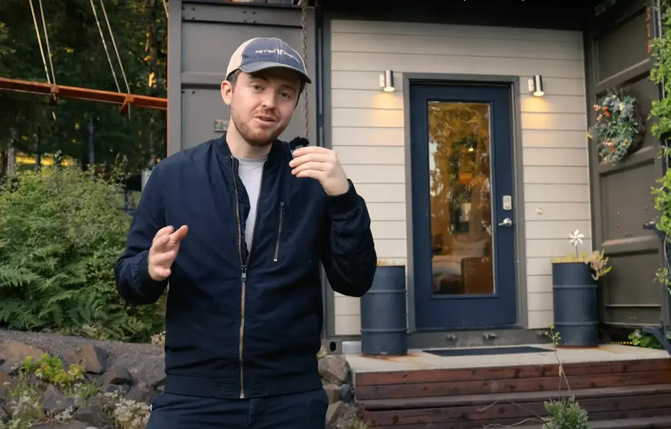 YouTube host presenting Highland & Co. Acres tiny home accommodation with modern exterior design and forest setting during video feature